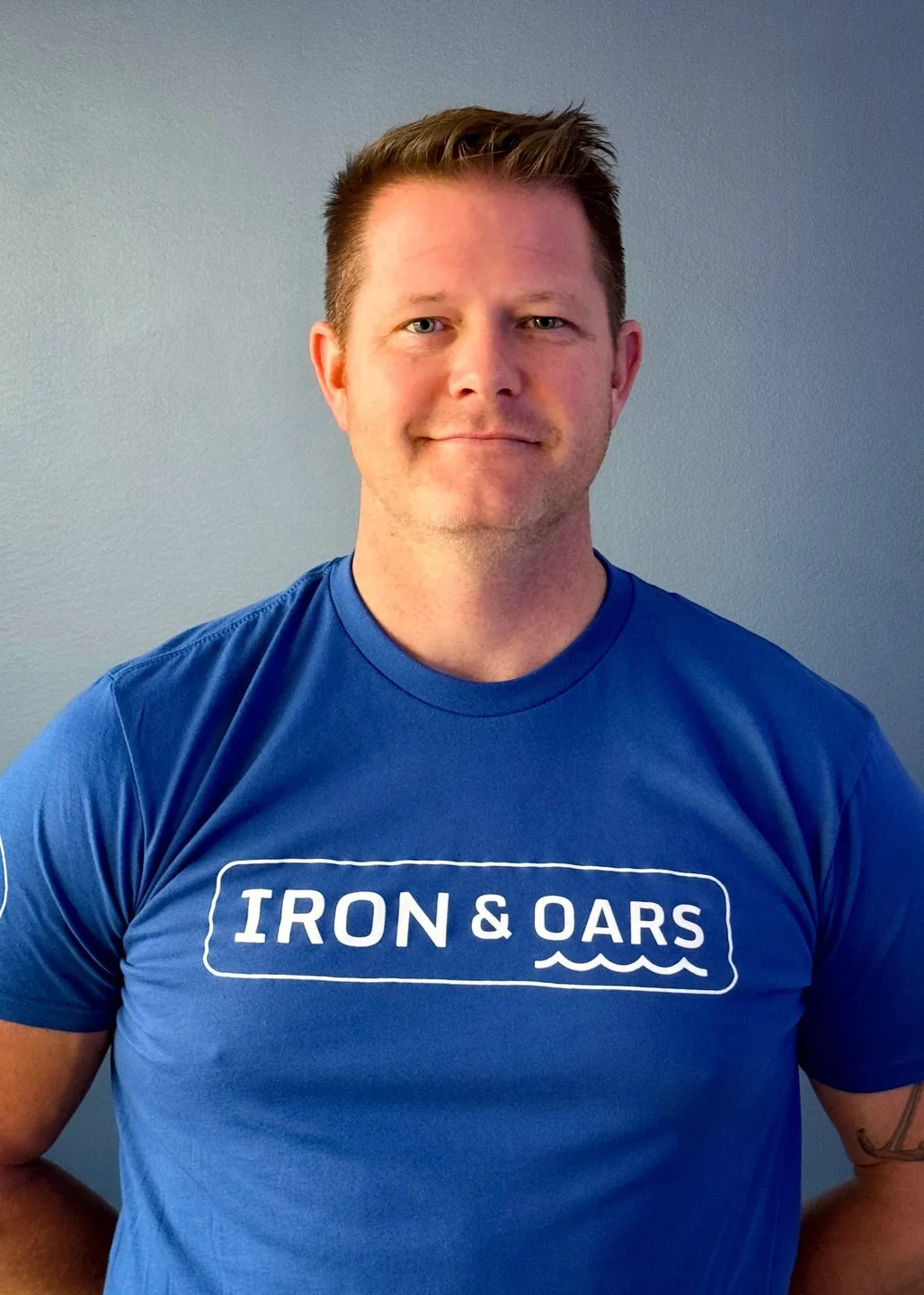 A man wearing a blue shirt with the words " iron & oars ".